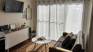 A living room with a sofa, a coffee table, a TV mounted on the wall, and a window with sheer curtains. - Seascape Retreat: Time to Slow Down (Agnes Water)