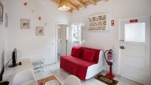 Una habitación con una cama, un escritorio con una computadora, una silla, un extintor y una puerta con letrero de salida de emergencia.