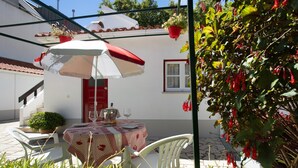 Un patio con una mesa, sillas, un paraguas rojo y blanco, y plantas en macetas.