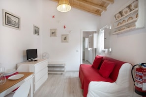 A room with a bed, a desk with a computer, a chair, a small table with plates and glasses, and a fire extinguisher.