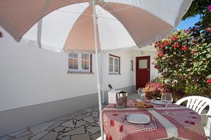 An outdoor table set with a tablecloth, a pitcher, plates, and glasses, under a large umbrella.