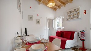 Un área de comedor con una mesa preparada para cuatro personas, un sofá rojo y un extintor de incendios montado en la pared.