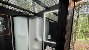 A modern bathroom with a glass shower enclosure, a wooden vanity with a sink, and a view of a forested area. - Mirrored Lost Lake Dome In Cosby - Your Ultimate Hideaway! (Cosby)
