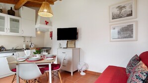 A modern kitchen with white cabinets, a dining table set with plates and glasses, a TV mounted on the wall, and a red sofa in the living area.