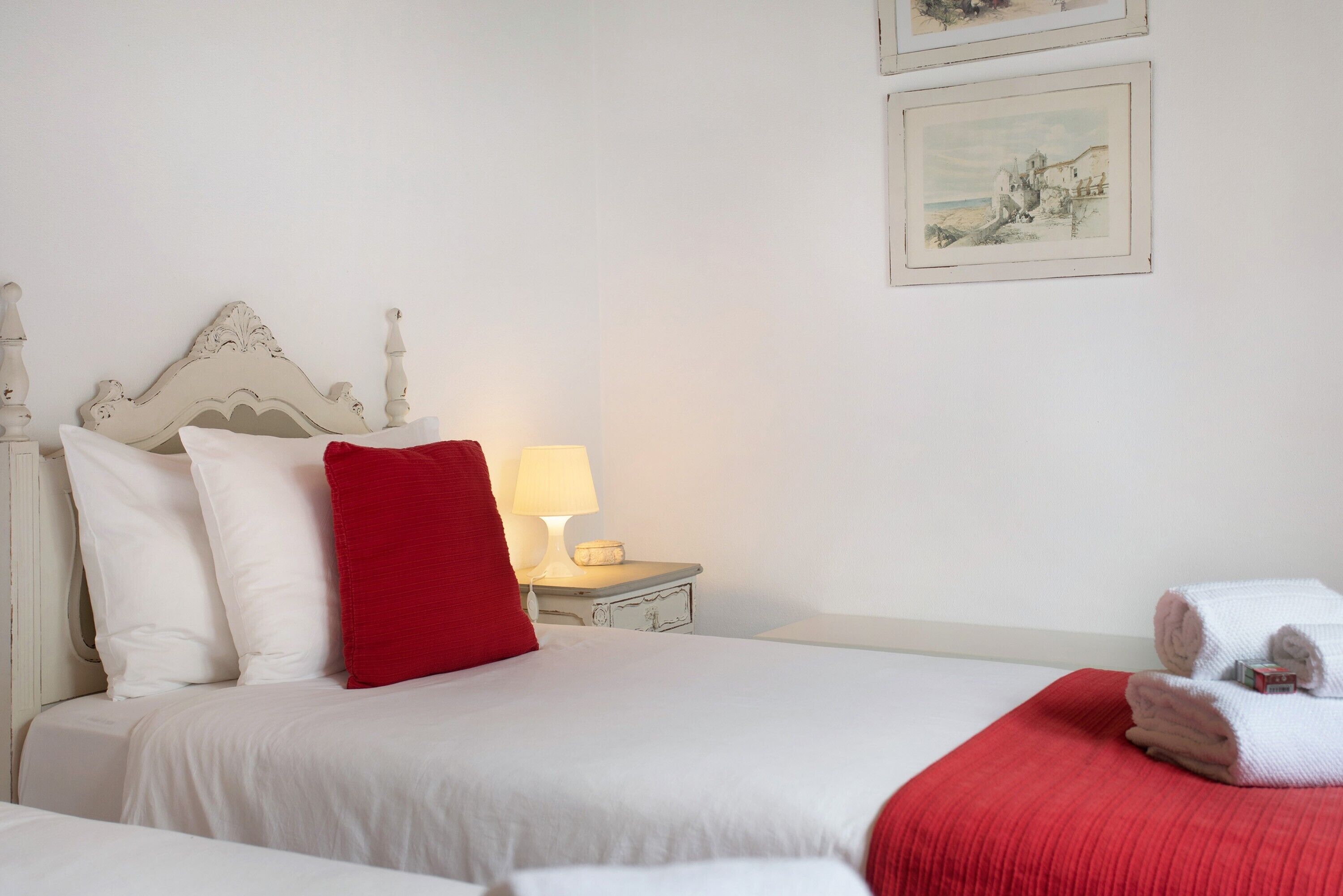 A neatly made bed with white and red bedding, a bedside lamp, and a small bedside table with a lamp.