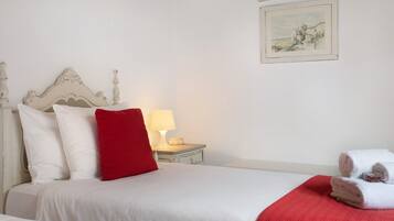 A neatly made bed with white and red bedding, a bedside lamp, and a small bedside table with a lamp.