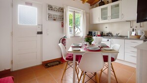 A kitchen with white cabinets, a dining table with chairs, a fire extinguisher, and a window with curtains.