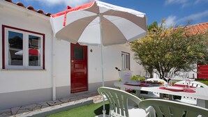 A white building with a red door, a white umbrella, and outdoor dining chairs.
