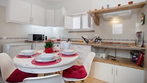 Una cocina moderna con armarios blancos, una mesa de comedor para cuatro personas y un microondas.
