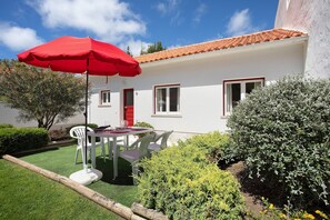 Un bâtiment blanc avec un toit rouge, un parasol rouge et une table entourée de chaises dans le jardin.