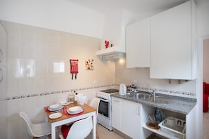A compact kitchen with white cabinets, a built-in oven, a countertop with a kettle, and a dining area with a table set for two.
