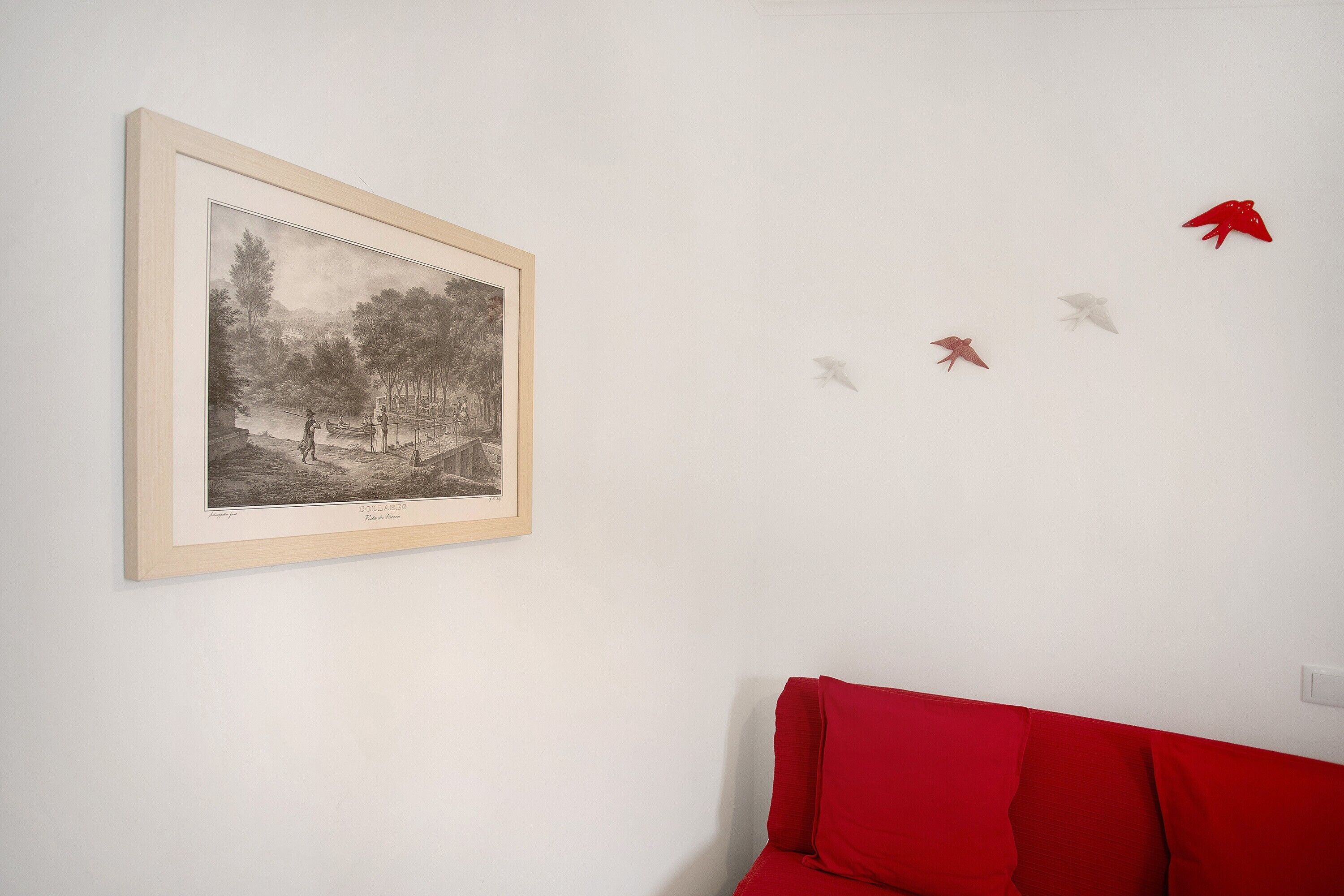 A framed black and white landscape painting, a red sofa, and a wall with paper airplanes.
