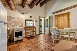 A kitchen with a stove, oven, and tiled backsplash. There is a wooden table and chairs, and a wooden door.