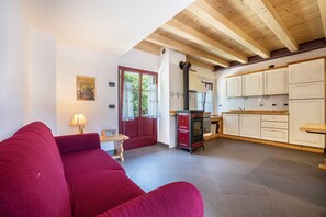 A living room with a red sofa, a wooden ceiling, and a kitchen with white cabinets.