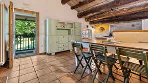 Een keuken met een houten plafond, een eettafel met stoelen, en uitzicht door een deur op een balkon.