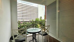 En balkon med et bord og stole, udsigt til en skyskraber, og et palmetræ.