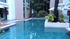 En swimmingpool med fliset gulv, omgivet af plantet blomster og en bygning med et skilt.