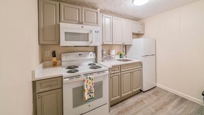 A compact kitchen with white appliances, including a stove, microwave, and refrigerator, and light-colored wooden cabinets. - Renovated 1-Bedroom Apartment in Beautiful Downtown Falmouth Located on Main St (Falmouth)