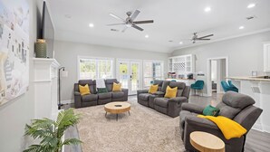 Ein geräumiges Wohnzimmer mit grauen Sofas, einem runden Couchtisch und einem Deckenventilator.