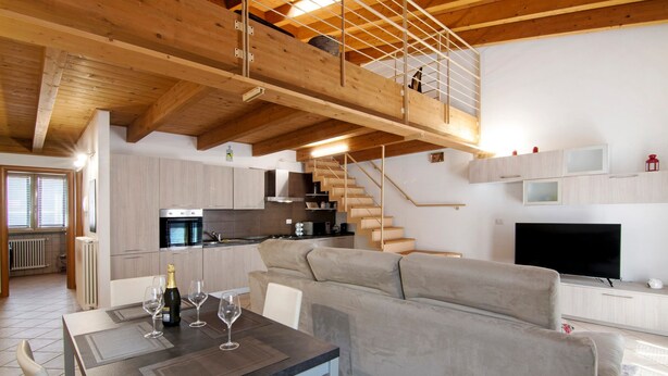A modern kitchen with wooden beams, a dining area with a table set for two, and a living area with a sofa and TV. - Apartment 'Casa Zia Dani' with Mountain View, Private Terrace and Wi-Fi (Piantedo)
