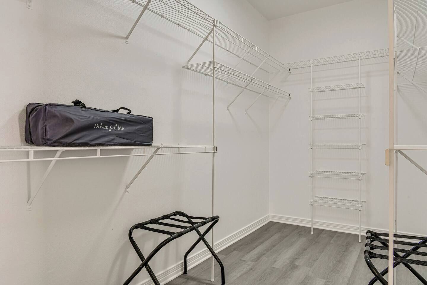 Un dressing ouvert avec des étagères métalliques, une tringle à vêtements et un tabouret en métal noir.