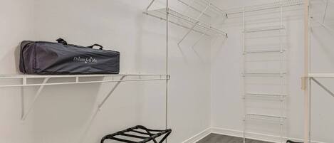 Un dressing ouvert avec des étagères métalliques, une tringle à vêtements et un tabouret en métal noir.