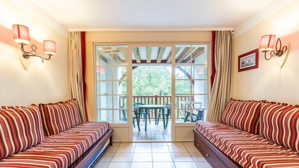 A room with two striped sofas facing a glass door leading to an outdoor area with a table and chairs. - Close to the lake, beautiful apartment residence with swimming pool (BISCARROSSE)