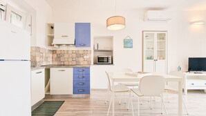 A modern kitchen with white cabinets, a blue upper cabinet, a patterned backsplash, and a dining area with a white table and chairs. - Apartment 'Bilo Terrazza Rio Elba' with Mountain View, Balcony and Air Conditioning (Rio Nell'elba)
