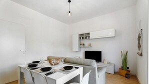 Ein modernes Wohnzimmer mit Essbereich, einer Couch, einem Flachbildfernseher und einem Blumentopf.