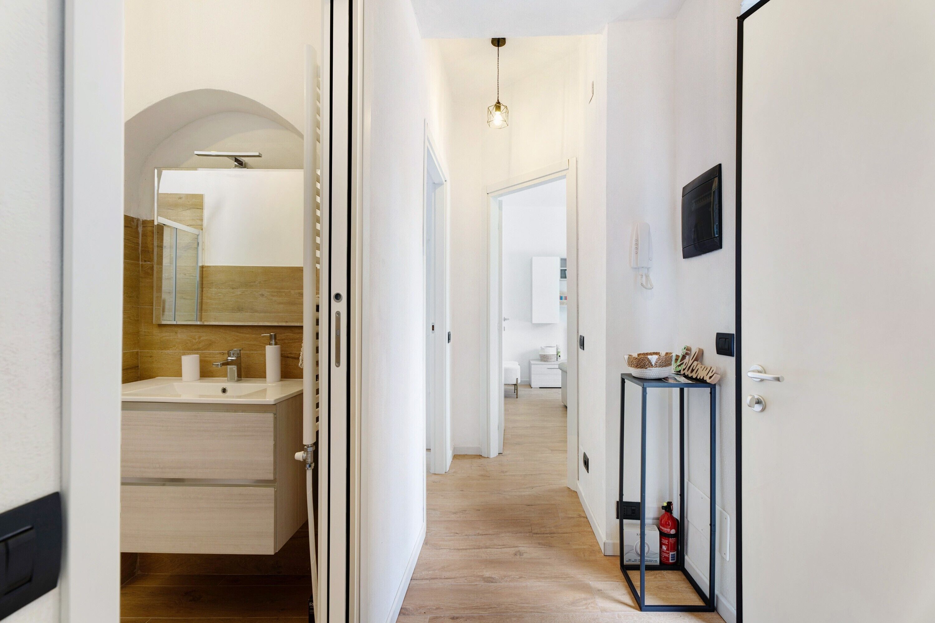Un couloir avec des toilettes sur la gauche, une porte avec une pancarte de bienvenue sur la droite et un extincteur posé sur le sol.