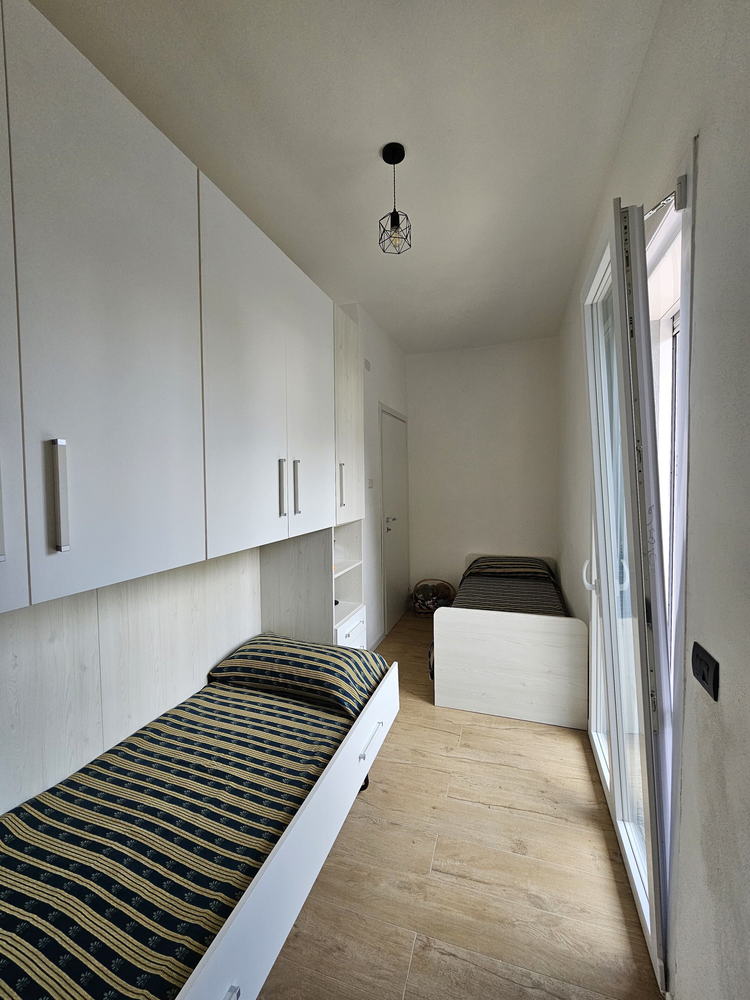 A narrow room with a bed, a wardrobe, and a window.