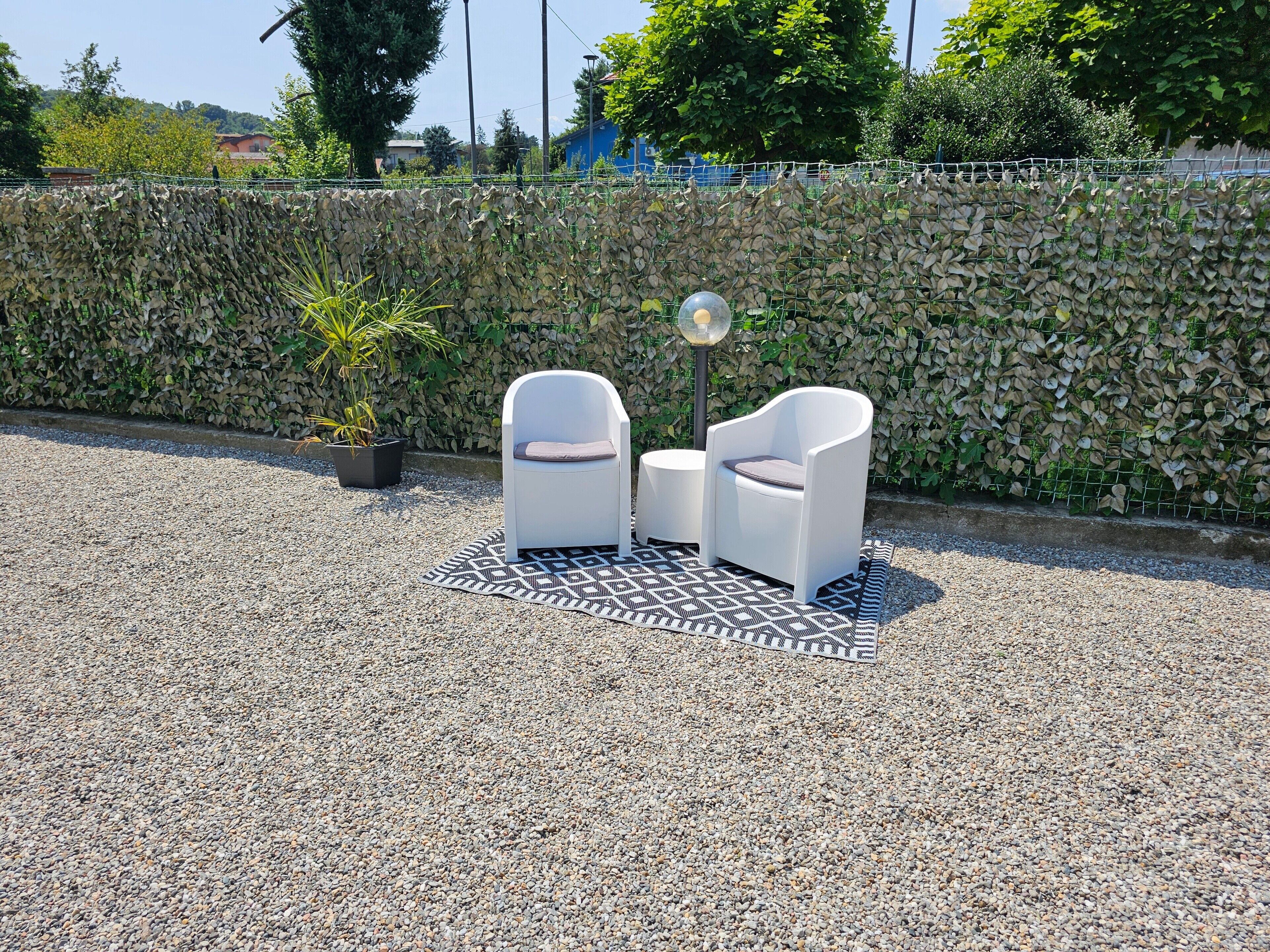 Un espace extérieur aménagé avec deux chaises blanches et une table, un tapis à motifs et une plante en pot.