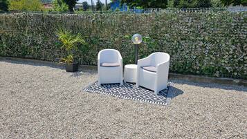 Un espace extérieur aménagé avec deux chaises blanches et une table, un tapis à motifs et une plante en pot.