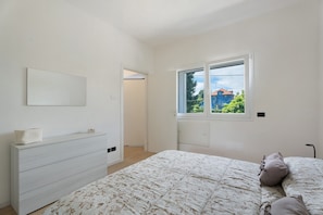 A bedroom with a bed, a dresser, a window with a view, and a door leading to another room. - Holiday Home 'Villa Lilia Appartamento Blu' with Shared Garden, Balcony and Wi-Fi (Arona)
