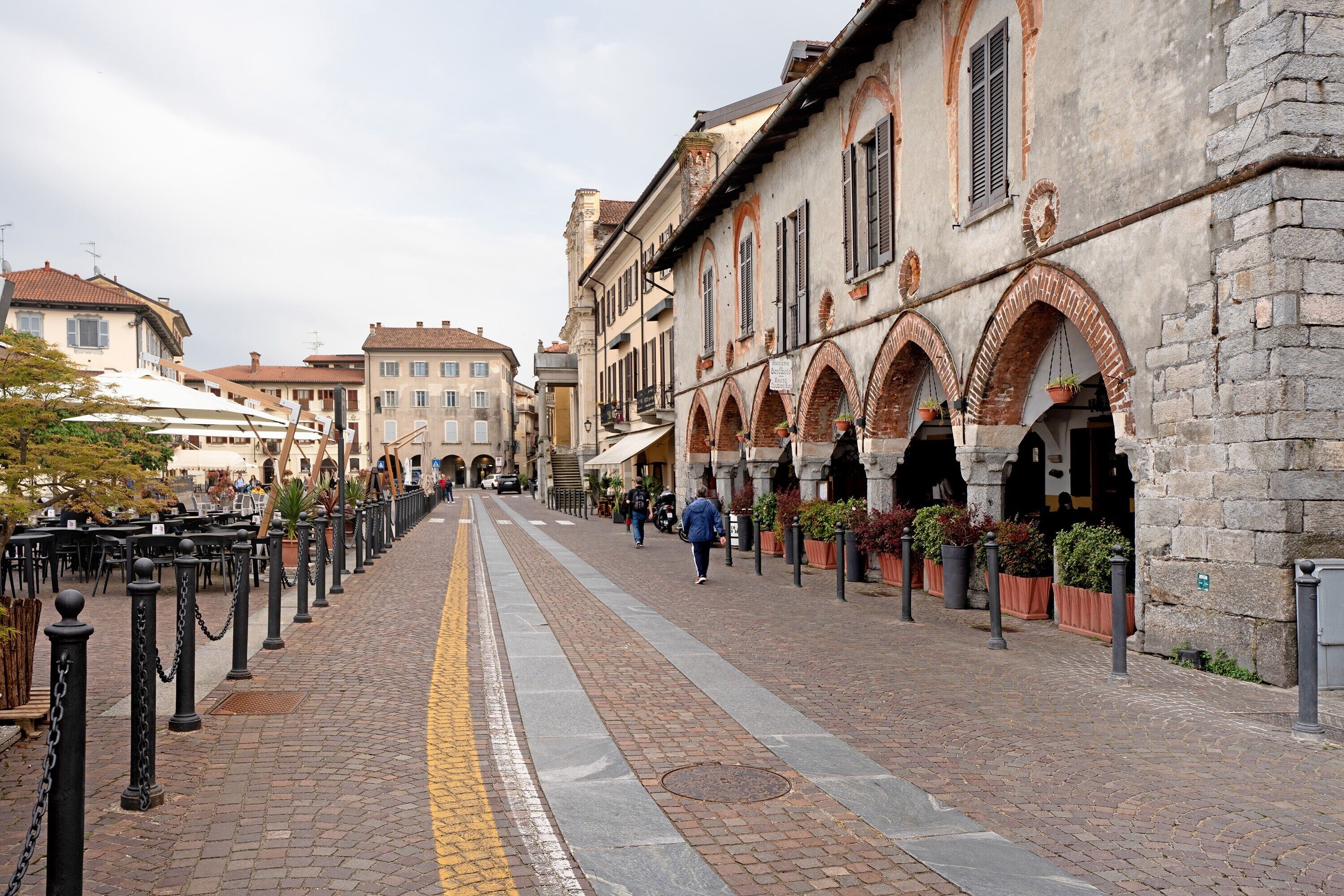 A cobblestone street lined with historic buildings, outdoor seating, and potted plants.