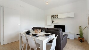 Ein modernes Wohnzimmer mit Esstisch für vier Personen, einer Couch, einem Flachbildfernseher und einem Blumentopf.