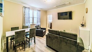 Ein Wohnzimmer mit Esstisch, Stühlen, Sofas und einem an der Wand befestigten Fernseher.