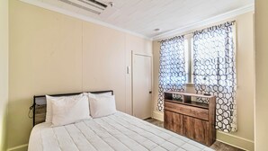 Ein Schlafzimmer mit einem Bett, einem Schminktisch, einem Fenster mit gemusterten Vorhängen und einer Klimaanlage an der Decke.