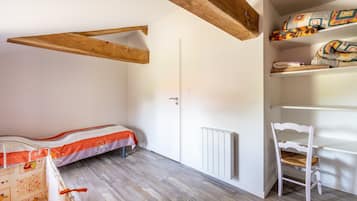 Une pièce comprenant un lit, une chaise, un radiateur et une étagère avec des couvertures pliées.