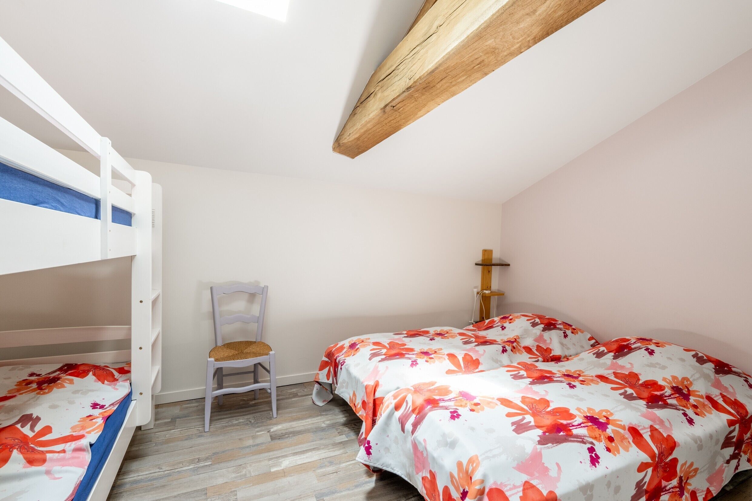 A bedroom with bunk beds, a chair, and a bed with floral bedding.