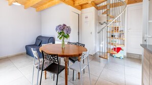 Un comedor con una mesa y sillas de madera, un jarrón de flores, un sofá azul y una escalera de caracol.