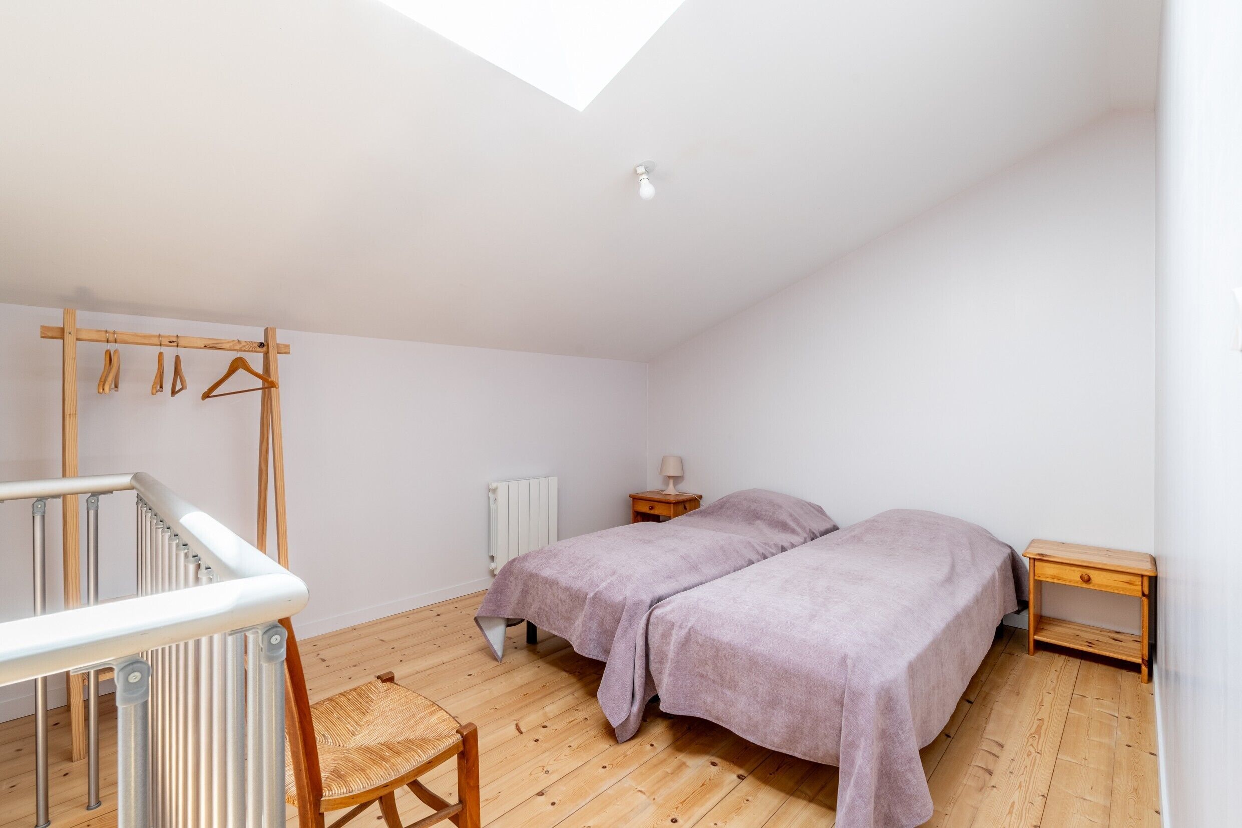 Un dormitorio con tragaluz, cama, silla, radiador y suelo de madera.
