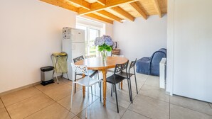 Una cocina con una mesa de madera, sillas, un cubo de basura, un refrigerador y una ventana.