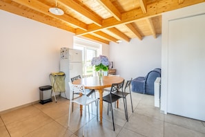 A kitchen with a wooden table, chairs, a trash bin, a refrigerator, and a window.
