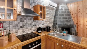 Une cuisine avec un mur de protection en pierre, des armoires en bois, une cuisinière encastrée et une cheminée en pierre.