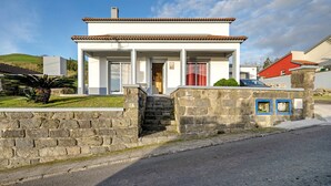 Une maison à deux étages avec une entrée surmontée d’un mur en pierre, un toit recouvert de tuiles et une porte bien visible.