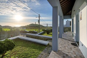 Uma área externa coberta com chão de pedra, gramado e vista para o campo.