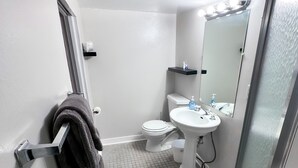 A bathroom with a toilet, sink, and mirror. There is a towel rack with a towel hanging on it. - The Downtown Hobbit Hole (Tacoma)