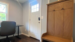Een kamer met een houten bank, een witte deur met raam, een zwarte bureaustoel en een kleine tafel.
