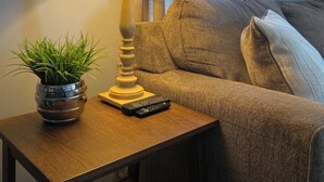 Een lamp, een afstandsbediening en een bloempot met plant op een houten bijzettafeltje naast een bank.